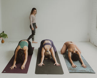 Calm group yoga class in a bright minimalist studio — instructor watching three students on mats practicing child's pose.
