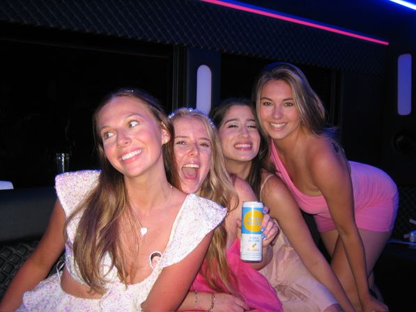 Four smiling young women enjoying a neon-lit party bus night out, laughing and posing together while one holds a canned vodka seltzer.