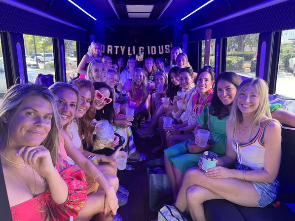 Smiling group of women holding drinks inside a purple LED-lit party bus, enjoying a girls' night out celebration.