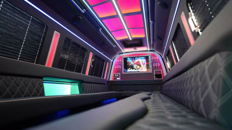 Luxurious party limo interior with quilted leather bench seating, vibrant pink and blue LED ceiling panels and strip lighting, flat-screen TV showing an aquarium, and window blinds.