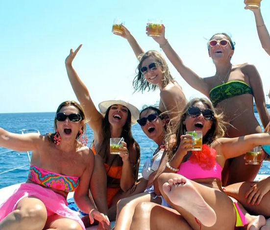 Boat party with a group of friends in colorful swimwear cheering and raising cocktails on a sunny day at sea
