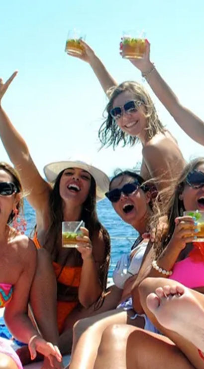 Boat party with a group of friends in colorful swimwear cheering and raising cocktails on a sunny day at sea