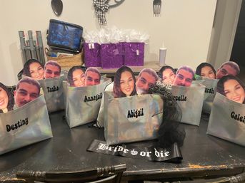 Iridescent personalized gift bags with large cutout face props and visible names on a dining table, purple glitter gift boxes and a “Bride or Die” sash — bachelorette party favors in a home setting.