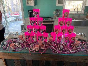 Bright pink bachelorette party setup on a kitchen island: two pyramids of dog-themed neon cups, mini liquor bottles, 'Team Bride' cups, beads, straws, sashes and other party favors.