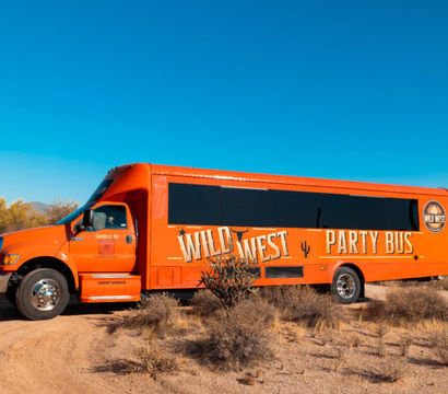 Bright orange western-themed party bus parked on a desert dirt road amid saguaro cacti under a clear blue Arizona sky