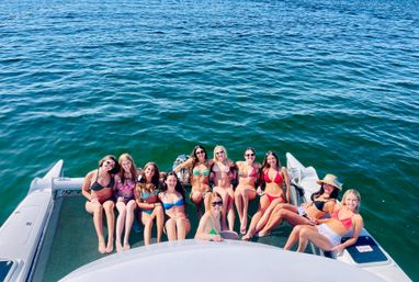 Group of women in colorful bikinis relaxing and smiling on the rear netting of a boat over bright blue open water on a sunny summer day