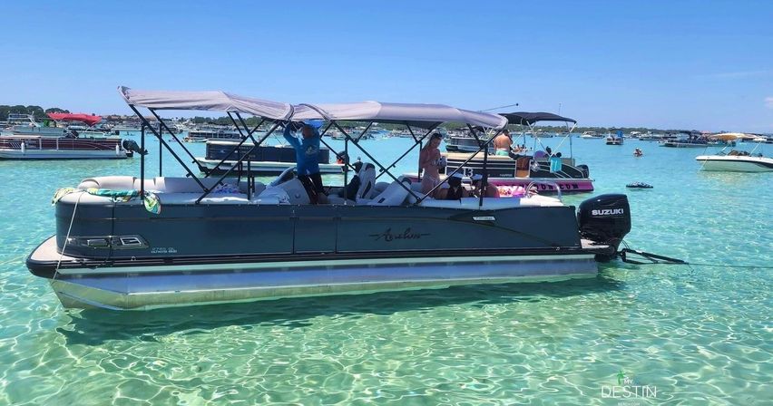 Pontoon boat with shaded canopies and people anchored in crystal-clear turquoise water near Destin, Florida, with other boats dotting the sunny horizon