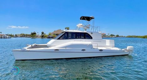 White motor catamaran with flybridge and black bimini anchored in calm turquoise coastal waters near waterfront homes and mangroves under a clear blue sky
