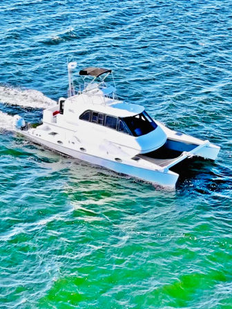 Aerial view of a sleek white catamaran motor yacht cruising turquoise coastal waters and leaving a foamy wake
