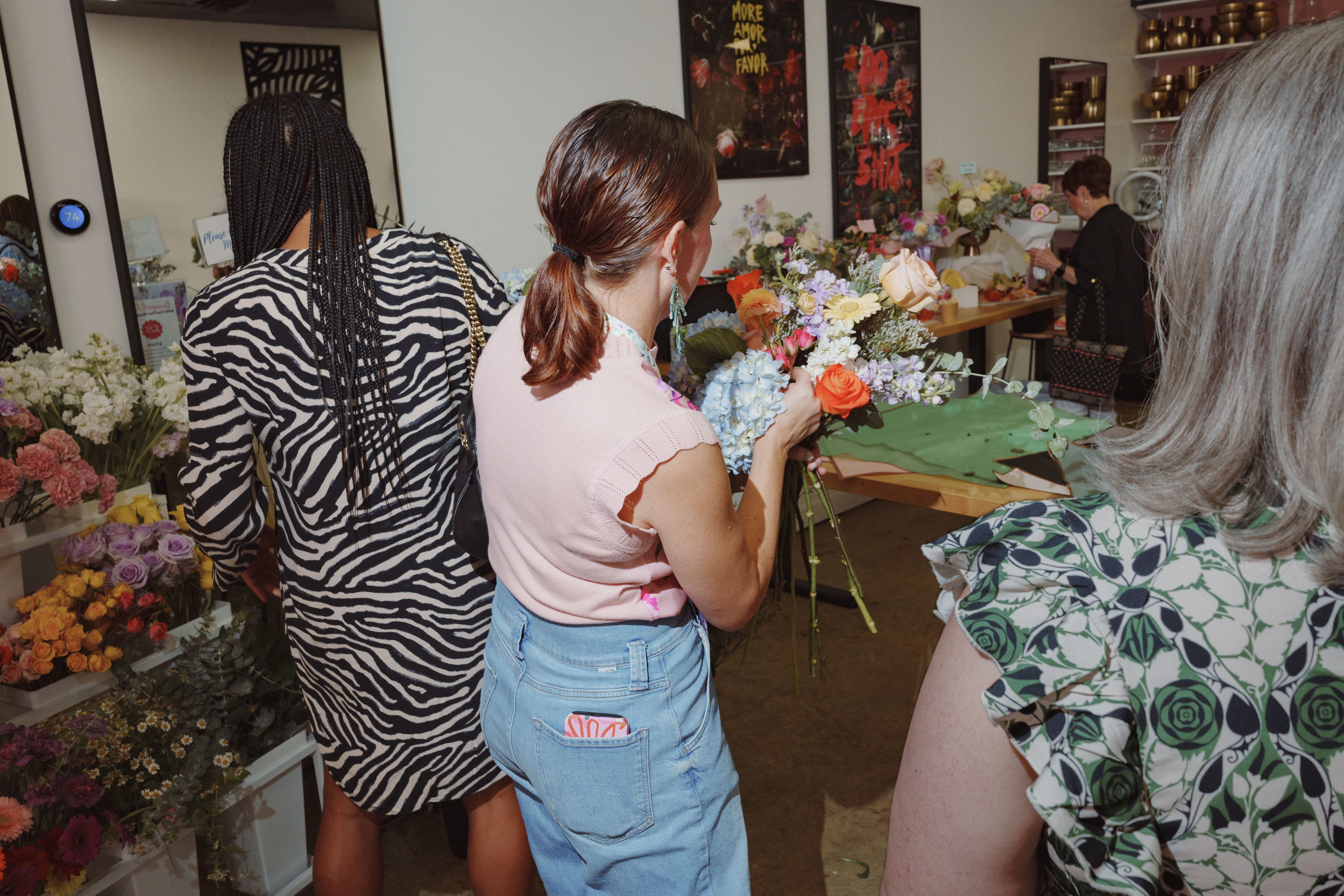 Hands-on floral workshop: people arranging a colorful bouquet in a bright studio surrounded by roses, hydrangeas and mixed greenery.