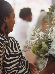Woman with braided hair in a zebra-print top holding a lush bouquet of hydrangeas, eucalyptus, and delicate filler flowers at an indoor event