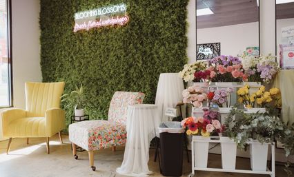 Bright boutique flower shop interior with moss wall and neon sign, yellow armchair, floral-patterned chair and colorful bouquets on white racks