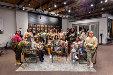 Smiling group portrait in an urban loft studio holding colorful bouquets after a community floral workshop.