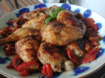 Golden roasted chicken thighs and drumsticks with blistered cherry tomatoes and fresh basil on a colorful Mediterranean-style serving plate
