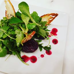Arugula and roasted beet salad with toasted crostini and bright magenta beet vinaigrette droplets on a white square plate