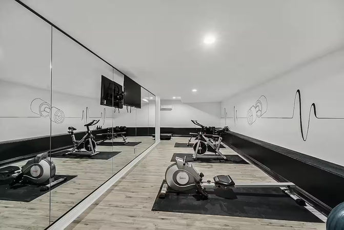 Compact modern fitness studio with mirrored wall and light wood floors, featuring spin bikes, a rowing machine, exercise mats and heartbeat-themed wall art — boutique indoor gym setup.