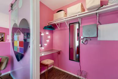 Bright pink dressing nook with a lighted heart-shaped mirror, velvet stool, floating vanity shelf, hanging rack and frosted heart sliding door
