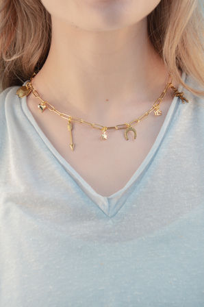 Close-up of a person's neck wearing a gold paper-clip chain charm necklace with arrow, star, horseshoe, heart and "YES" charms over a light blue V-neck tee.