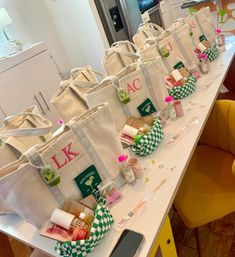 Personalized canvas tote gift bags with monogram initials, mini skincare items and green-check pouches neatly lined up on a bright kitchen island as party favors