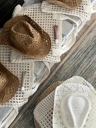 Flatlay of woven straw and white crochet sun hats, matching crochet tote bags and sunscreen tubes on a rustic coastal rug — boho beach essentials