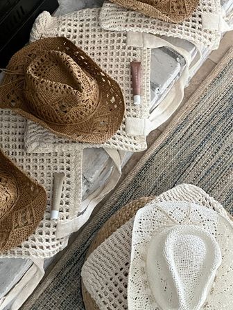 Flatlay of woven straw and white crochet sun hats, matching crochet tote bags and sunscreen tubes on a rustic coastal rug — boho beach essentials