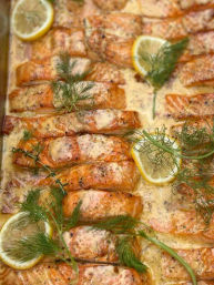 Golden oven-baked salmon fillets in creamy lemon-dill sauce, garnished with lemon slices and fresh dill on a baking tray