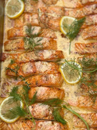 Golden oven-baked salmon fillets in creamy lemon-dill sauce, garnished with lemon slices and fresh dill on a baking tray