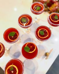 Overhead shot of sugar-rimmed coupe glasses filled with bright blood orange cocktails, each garnished with a blood orange slice and mint leaf on a white table