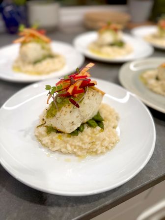 Seared white fish fillet with herb pesto atop creamy Parmesan risotto and sautéed greens, finished with carrot and red pepper ribbons and microgreens — plated for modern restaurant service.