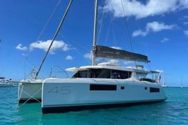 White 45-foot catamaran sailboat moored in clear turquoise tropical water under a sunny blue sky with scattered clouds