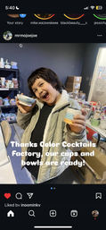 Excited child in a pottery studio holding two handmade painted ceramic bowls, with shelves of colorful cups, glazing tools and boxes in the background — kids pottery workshop scene.