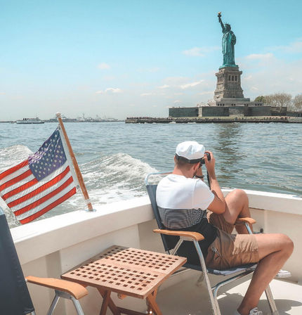 Person on a sightseeing boat with an American flag using binoculars to view the Statue of Liberty in New York Harbor on a sunny day