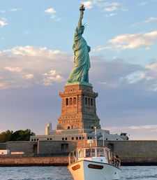 Sunlit Statue of Liberty on Liberty Island at golden-hour over New York Harbor with a small white tour boat in the foreground