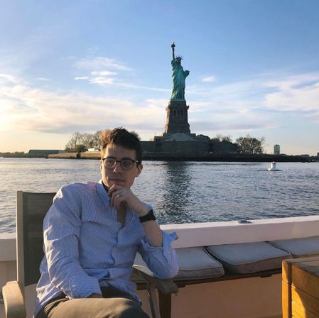 Person with glasses lounging on a boat with the Statue of Liberty on Liberty Island rising over New York Harbor at golden hour