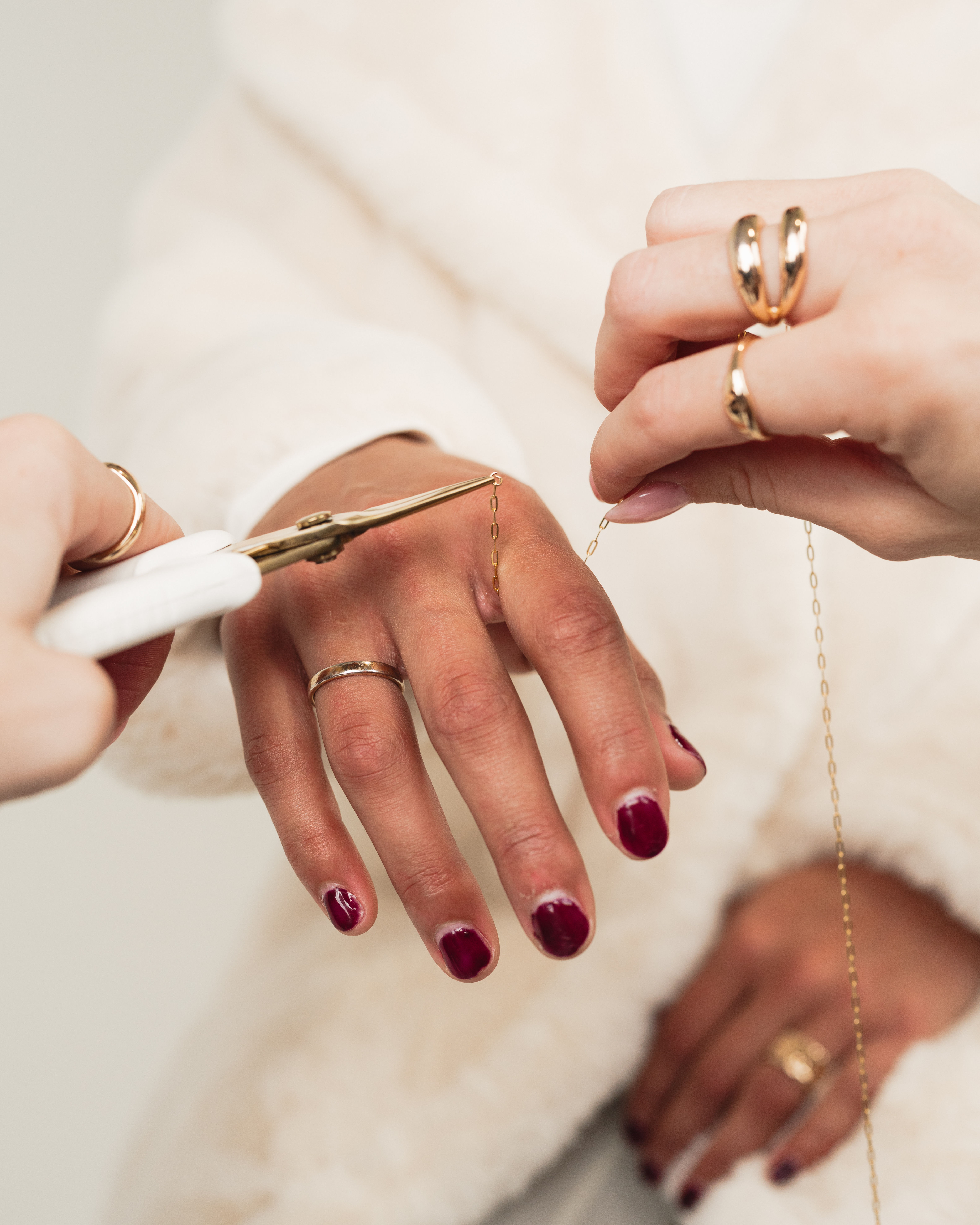 Close-up of hands with burgundy nails and gold rings as a jeweler uses pliers to adjust a delicate gold chain, jewelry repair scene