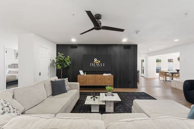Stylish contemporary open-plan living room with a light gray sectional, black slatted feature wall, wooden media console, marble coffee table, ceiling fan and dining area beyond