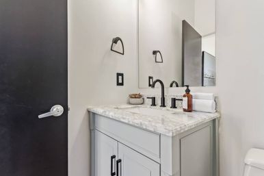 Contemporary powder room with light-gray vanity and marble countertop, matte-black faucet and hardware, rectangular mirror, amber soap dispenser, rolled white towel and small succulent on the counter.