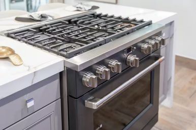 Sleek stainless steel gas range with cast-iron grates, chrome control knobs and oven door set into a white marble countertop kitchen island in a contemporary home