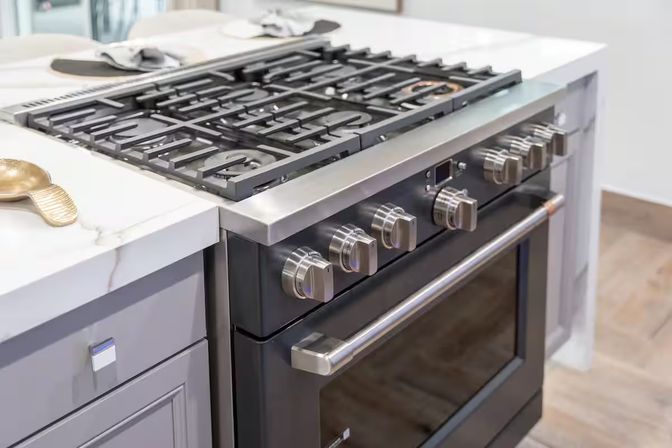Sleek stainless steel gas range with cast-iron grates, chrome control knobs and oven door set into a white marble countertop kitchen island in a contemporary home