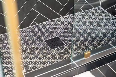 Modern bathroom shower floor with black-and-white geometric star tiles, square center drain, glass door panel and small brass accent