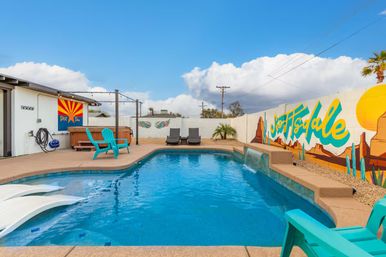 Turquoise backyard pool in Scottsdale with a small waterfall edge, lounge chairs, hot tub, string lights and a colorful desert mural on the privacy wall.