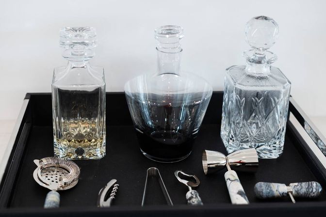 Three crystal decanters and cocktail tools on a black tray — elegant home bar setup for spirits and cocktails.