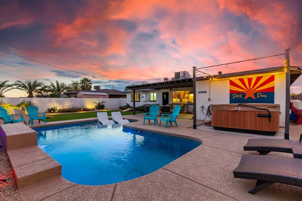 Backyard swimming pool and hot tub with lounge chairs and turquoise patio seating in front of a house under a vibrant Arizona sunset and wall mural.
