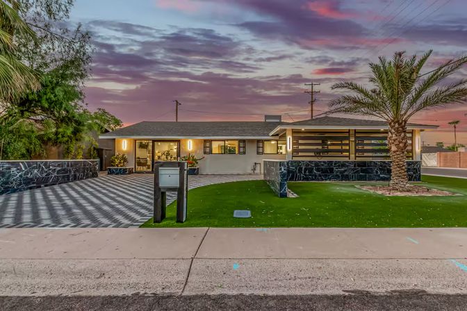Mid-century modern single-story suburban home with patterned driveway, marble accent walls, palm tree and vibrant sunset sky.