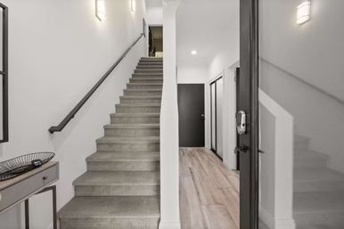 Contemporary home entryway with carpeted staircase, wood-look plank flooring, wall sconces, minimalist console table and electronic keypad front door lock