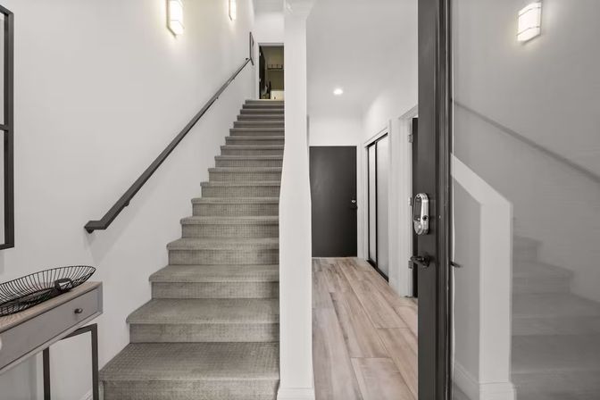 Contemporary home entryway with carpeted staircase, wood-look plank flooring, wall sconces, minimalist console table and electronic keypad front door lock