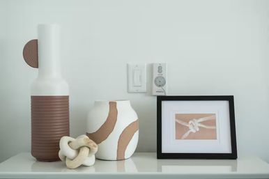 Modern minimalist home decor on a shelf: ribbed brown-and-white ceramic vases, a decorative knot sculpture, and a black-framed knot photo against a pale wall in neutral tones.