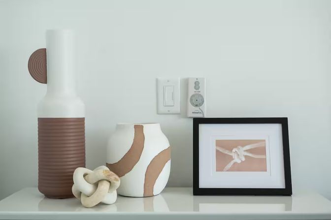 Modern minimalist home decor on a shelf: ribbed brown-and-white ceramic vases, a decorative knot sculpture, and a black-framed knot photo against a pale wall in neutral tones.