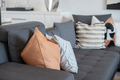 Close-up of a modern gray sectional sofa in a contemporary living room, styled with textured tan, striped white, and black-and-white patterned throw pillows.