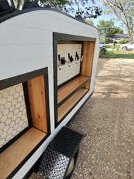 Mobile bar trailer with four beer taps, honeycomb tile backsplash and wooden shelves, parked on a gravel driveway under trees
